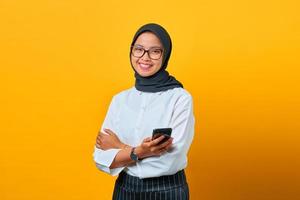 lächelnde junge asiatische frau mit handy und sms auf gelbem hintergrund foto
