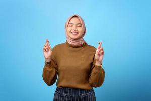 Porträt einer glücklichen jungen asiatischen Frau, die den Finger auf blauem Hintergrund kreuzt foto