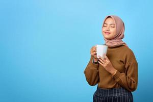 schöne junge asiatische frau, die becher hält und tee auf blauem hintergrund trinkt foto