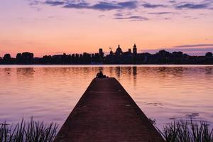 Paar sitzt am Pier und schaut auf den Sonnenuntergang und die Skyline der Stadt foto