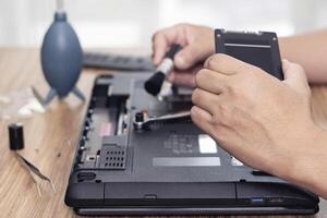 Computer Alphabetisierung Reparatur Männer Hände halten schwer Platte von Laptop zum prüfen Reparatur und Reinigung mit Computer Reparatur Werkzeuge auf Tabelle foto