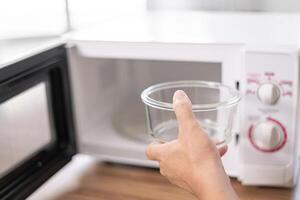 schließen oben Hand ein Mann platziert ein leeren Glas Schüssel im Mikrowelle Ofen zu Koch im das Küche Essen Konzept Foto