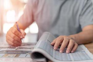 mann, der die zeitung nach einem neuen job sucht und mit stift in notizbuch zu hause schreibt, während er zu hause arbeitet foto