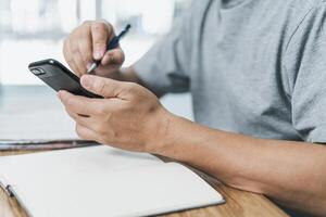 männlich halt Smartphone suchen Nachrichten online finden Job Anwendungen mit Zeitung und schreiben im Notizbuch auf Holz Tabelle foto