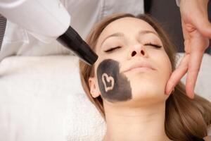 Kosmetikerin tut Verfahren von Kohlenstoff Peeling von Gesicht. schwarz Maske, Laser- Haut Reinigung. modern Behandlungen. Prozess foto
