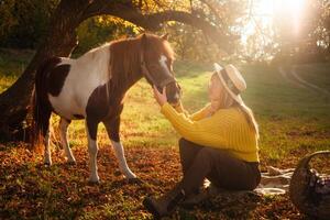 Frau und entdeckt braun Pony beim Sonnenuntergang im Wald, schön Mädchen im Herbst Kleider liebt ihr Pferd, Konzept von Freundlichkeit, Tier Pflege, Natur und Freundschaft. Hut. foto