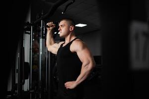 ein Sport Athlet Trainer ein muskulös Mann tut ein Übung auf ein Simulator im Fitnessstudio. Porträt, niedrig Taste, Dunkelheit. Bodybuilder foto