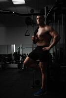 Porträt von ein schön männlich Athlet Bodybuilder im Fitnessstudio, niedrig Taste, Dunkelheit. posieren, Coach. Stehen foto