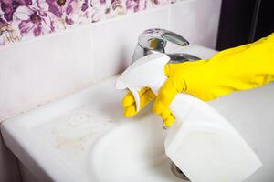 Maid mit Gummi Handschuh Reinigung Zapfhahn und Waschbecken. foto