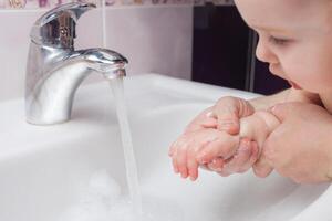 Kind wäscht Hände im Waschbecken. Jet von Wasser von klopfen. Desinfektion von Hände mit Wasser. foto