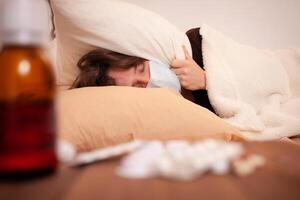 ein krank Mann im ein medizinisch Maske gegen das Hintergrund von Tablets. Zuhause Quarantäne, Coronavirus, Covid. das Mann ist bedeckt mit ein Kissen und schlafend foto