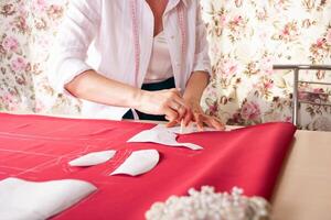 Näherin beim arbeiten. Schneider Herstellung Kleider im modern Studio. Schneider halten Bleistift und Markierung Stoff. Frau Stehen beim Tabelle mit Schnitt Textil, Nähen Maschine, Gewinde, Stifte, Nadeln, Band, Ausschnitte foto