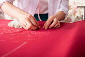 Näherin beim arbeiten. Schneider Herstellung Kleider im modern Studio. Schneider halten Bleistift und Markierung Stoff. Frau Stehen beim Tabelle mit Schnitt Textil, Nähen Maschine, Gewinde, Stifte, Nadeln, Band, Ausschnitte foto