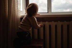 das Kind klettert zu das Fenster, das Mädchen auf das Fenster Schwelle ruht auf das Netz, das Achtung von fallen. das Kind ist allein beim heim, können fallen aus von das Fenster. foto