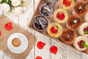 Süss Dessert im Glas mit Keks, Beere Obst und ausgepeitscht Creme. ein Tasse von Tee, Blumen, Kuchen im ein Kasten. Lieferung von Essen zu das Haus zum Parteien oder ein Abendessen foto