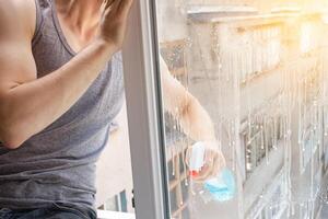 ein Mann wäscht ein Fenster von das außen. das Mann Sprays ein Blau Reiniger foto