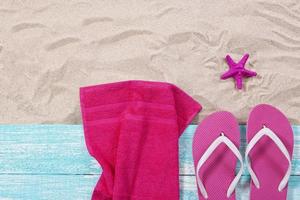 Sommerhandtücher, Flip-Flops und rosa Seesterne auf dem Sand Draufsicht foto