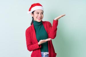 junge asiatische Frau mit Weihnachtsmütze auf grünem Hintergrund, Weihnachtskonzept foto