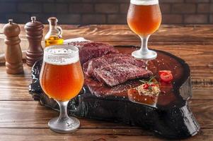 Gegrilltes Denver-Steak auf Holzbrett mit zwei verschwitzten kalten Tulipa-Gläsern Bier vom Fass. Marmorfleisch Rindfleisch. foto