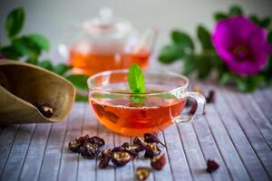 gebraut Hagebutte Tee im ein Glas Teekanne mit Hagebutte Blumen und Minze foto