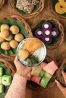 weiblich Hand stellen kue Basah traditionell indonesisch Essen jajanan Pasar zu Emaille Teller foto