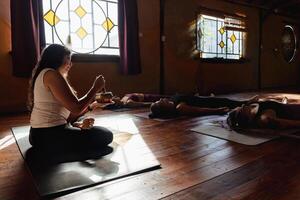 weiblich Yoga Lehrer Dirigieren ein Meditation Sitzung. Shavasana, das Haltung von Erleichterung, Schweigen, und Stille foto