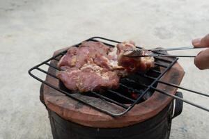 wählen oben ein Stück von frisch Schweinefleisch mit Stahl Zange. drei Stücke von gegrillt Schweinefleisch auf ein Gummi Grill. Platz auf das Holzkohle Herd. foto