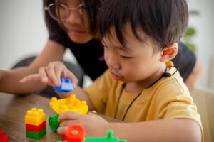 asiatisch süß Bruder und Schwester abspielen mit ein Spielzeug Block Designer auf das Tabelle im das Leben Zimmer beim heim. Konzept von Geschwister Verbindung, Freundschaft, und Lernen durch abspielen Aktivität zum Kind Entwicklung. foto