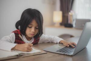 süß und glücklich wenig asiatisch Mädchen Kinder mit ein Laptop Computer, studieren durch ein online E-Learning System beim heim. foto