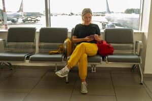 Flughafen Terminal. Frau warten zum Flug mit Smartphone. Mädchen mit Zelle Telefon im Flughafen Surfen Internet Sozial Medien Anwendungen. Reisen weiblich im Einsteigen Salon von Fluggesellschaft Hub. Reisen Mädchen foto