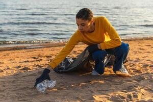 Erde Tag. Freiwillige Aktivisten Mannschaft sammelt Müll Reinigung von Strand Küsten Zone. Frau setzt Plastik Müll im Müll Tasche auf Ozean Ufer. Umwelt Erhaltung Küsten Zone Reinigung foto