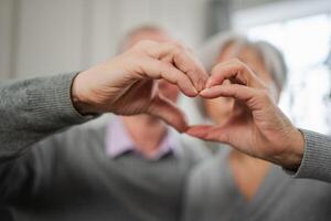 Liebe Herz gestalten Frieden. Senior älter Paar Herstellung Herz gestalten mit ihr Hände. Erwachsene reifen alt Mann Ehefrau zeigen Herz unterzeichnen. glücklich Rentner Familie. ich Liebe Sie glücklich Valentinsgrüße Tag foto