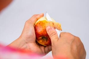 Hand Peeling Apfel mit Messer schließen hoch. Frau Peeling ein rot Apfel im das Küche. foto