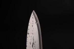 Wasser fallen auf Scharf Messer isoliert auf dunkel Hintergrund. Wasser planschen auf Messer. foto