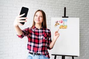 junge Künstlerin macht ein Selfie mit ihrem Bild foto