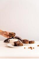 hausgemachte Schokoladen-Cupcakes mit Glasur, Walnüssen und einer Tasse Kaffee auf der Vorderansicht des weißen Tisches foto