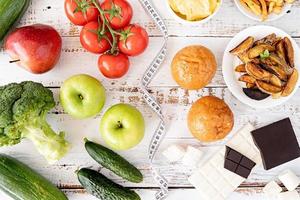 gesundes und ungesundes lebensmittelkonzept. Obst und Gemüse gegen Süßigkeiten und Kartoffelpommes Draufsicht flach auf Holzhintergrund foto