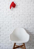 minimales Interieur mit einem Stuhl und einer roten Weihnachtsmütze, die an der weißen Backsteinmauer hängt