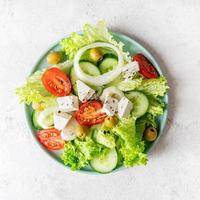 Griechischer Salat mit Feta-Käse, frischem Gemüse und Oliven auf weißem rustikalem Hintergrund Draufsicht quadratische Ausrichtung