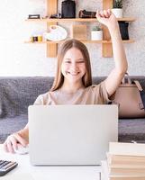 weiblicher Teenager, der von zu Hause aus am Schreibtisch mit erhobenem Arm sitzt foto