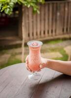 oben Aussicht von Hand halten ein Erdbeere Milchshake auf Tisch, Hände zeigen Erdbeere Smoothie auf hölzern Tisch. Hände halten Erdbeere Smoothie auf hölzern Tabelle mit verschwommen Hintergrund foto