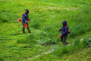 zwei kommunale Rasenmäher Männer mit Zeichenfolge Trimmer Trimmen Gras beim sonnig Tag foto