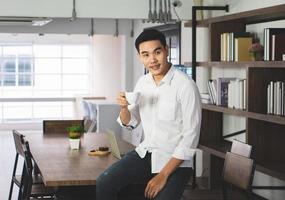 asiatischer Mann, der im Café sitzt, Kaffee trinkt und frühstückt und aus der Ferne aufwacht. Geschäfts- und Technologiekonzept