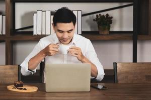 asiatischer Mann, der im Café sitzt, Kaffee trinkt und frühstückt und aus der Ferne aufwacht. Geschäfts- und Technologiekonzept