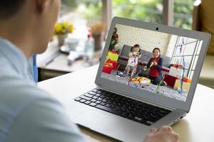 asiatischer Geschäftsmann, der im Büro in einem anderen Land arbeitet. Er benutzt Computer, um während der Weihnachts- und Neujahrsfeier mit der Familie Videoanrufe zu machen. neues normales und soziales Distanzierungskonzept foto