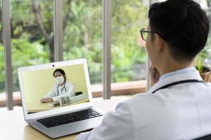 asiatischer Arzt konsultiert seinen Kollegen online per Videokonferenz über den Behandlungsplan des Patienten. telemedizinisches Konzept foto
