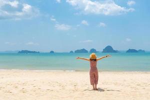 junge asiatische frau, die am strand steht und an einem sonnigen tag während der sommerferien auf das blaue meer schaut foto