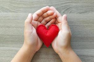 Hände halten ein rotes Herz aus Filz. foto