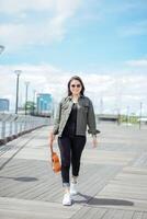 spielen Ukulele von jung schön asiatisch Frau tragen Jacke und schwarz Jeans posieren draußen foto
