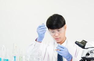 Porträt asiatisch Mann Schüler Wissenschaftler tragen ein Arzt Kleid im das Labor suchen Hand beim Chemiker. verursacht durch Mischen Reagenzien im wissenschaftlich Forschung Laboratorien mit Prüfung Röhren und Mikroskop auf das Tabelle foto